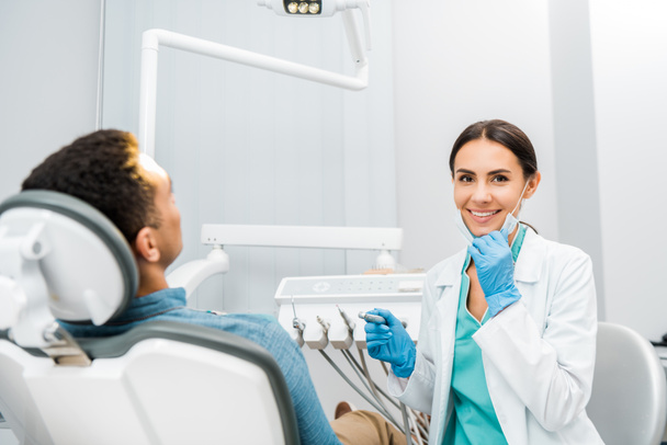 stock photo cheerful dentist holding drill smiling african american patient